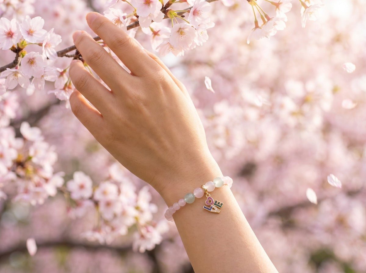 Rose Quartz LOVE Charm Bracelet on wrist under cherry blossom trees