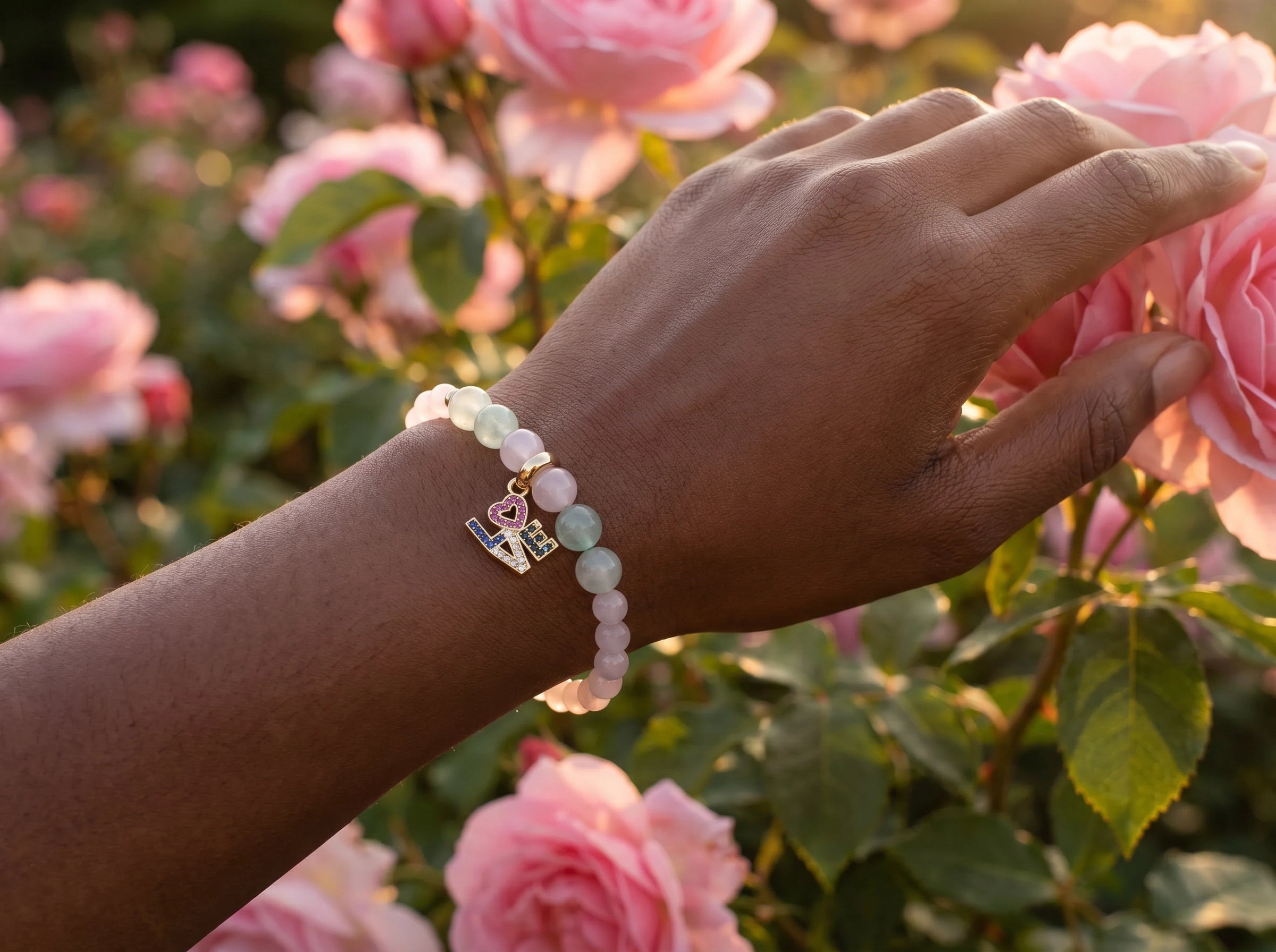 Rose Quartz LOVE Charm Bracelet on wrist in rose garden at golden hour